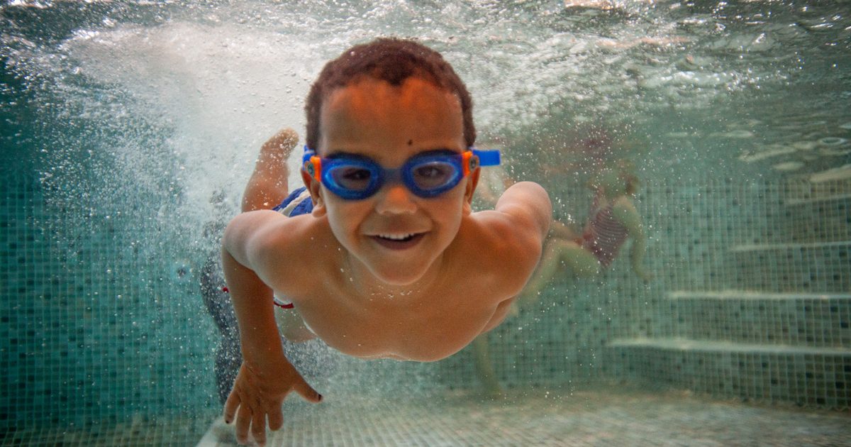 Boy swimming under water with goggles on.